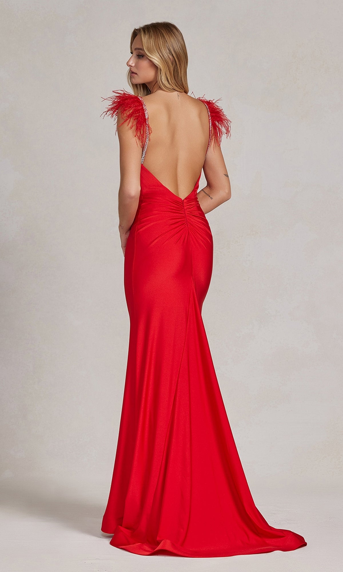 A woman faces away from the camera wearing the Feather-Embellished Backless Long Prom Dress, featuring a floor-length silhouette and feathered shoulder accents.
